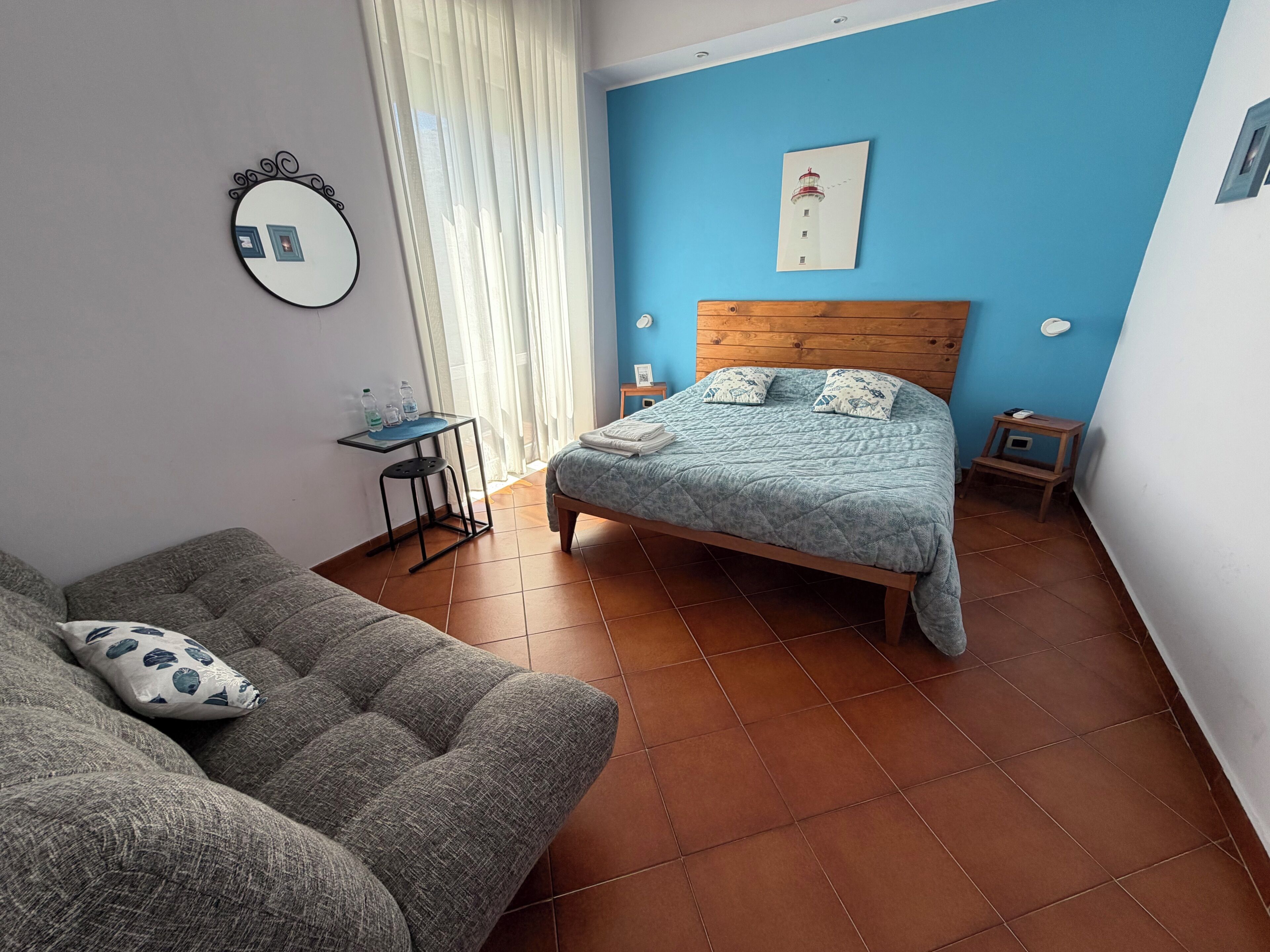 Une chambre à coucher avec un lit, une tête de lit en bois, une table de chevet, une petite table, une chaise et une fenêtre avec des rideaux.
