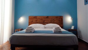 A neatly made bed with two pillows and two folded towels, a wooden headboard, and two bedside tables with lamps. - B&B Il Faro (Salerno)