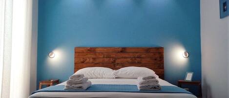 A neatly made bed with two pillows and two folded towels, a wooden headboard, and two bedside tables with lamps.