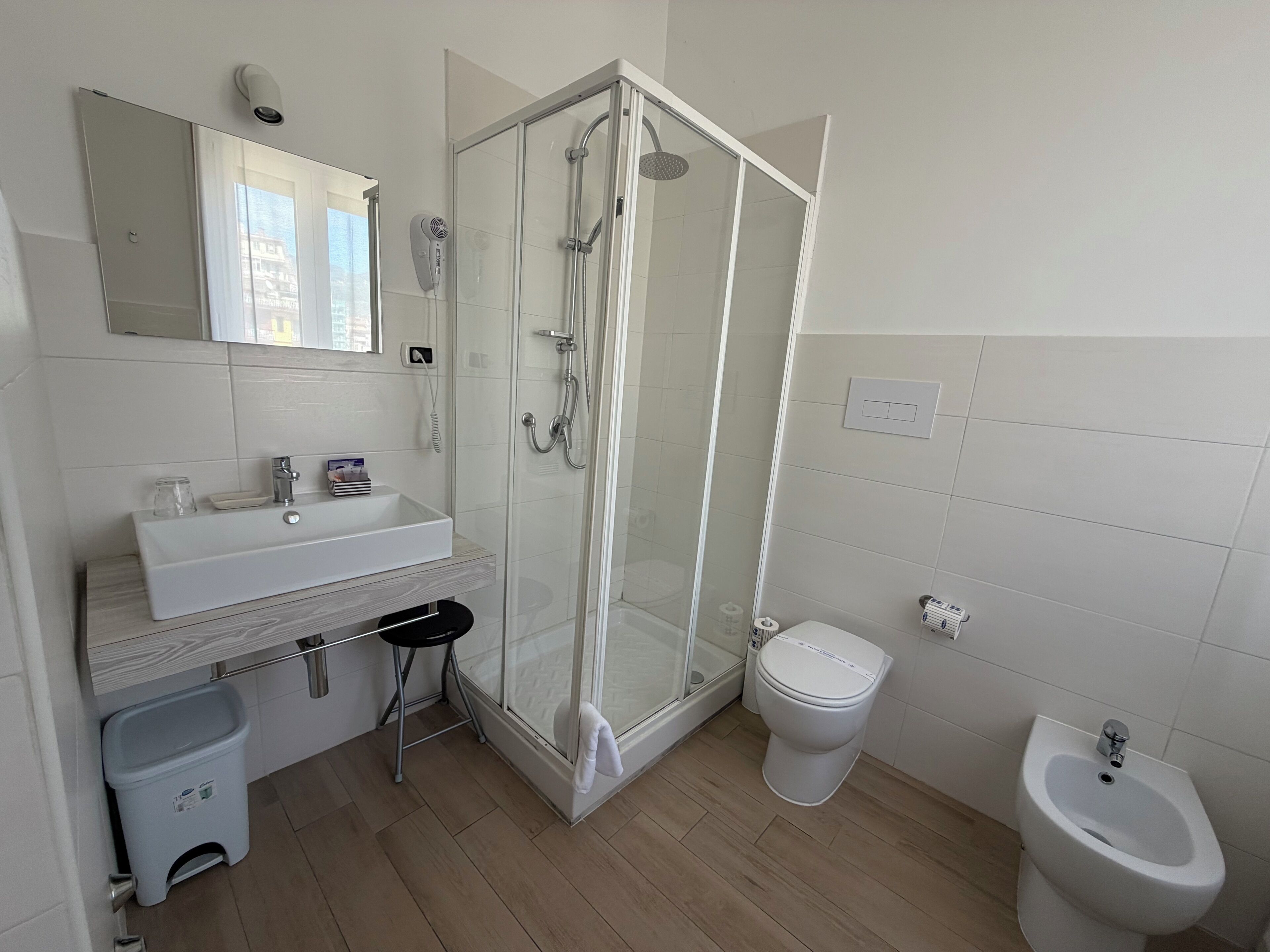 A modern bathroom with a glass-enclosed shower, a white sink, a toilet, and a bidet.