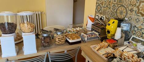 A breakfast buffet with various food items, including cereal, cookies, and pastries, and a coffee machine.