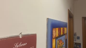 Un couloir avec un tableau encadré de rouge et de bleu accroché au mur, une porte et une petite fenêtre à l’arrière-plan.