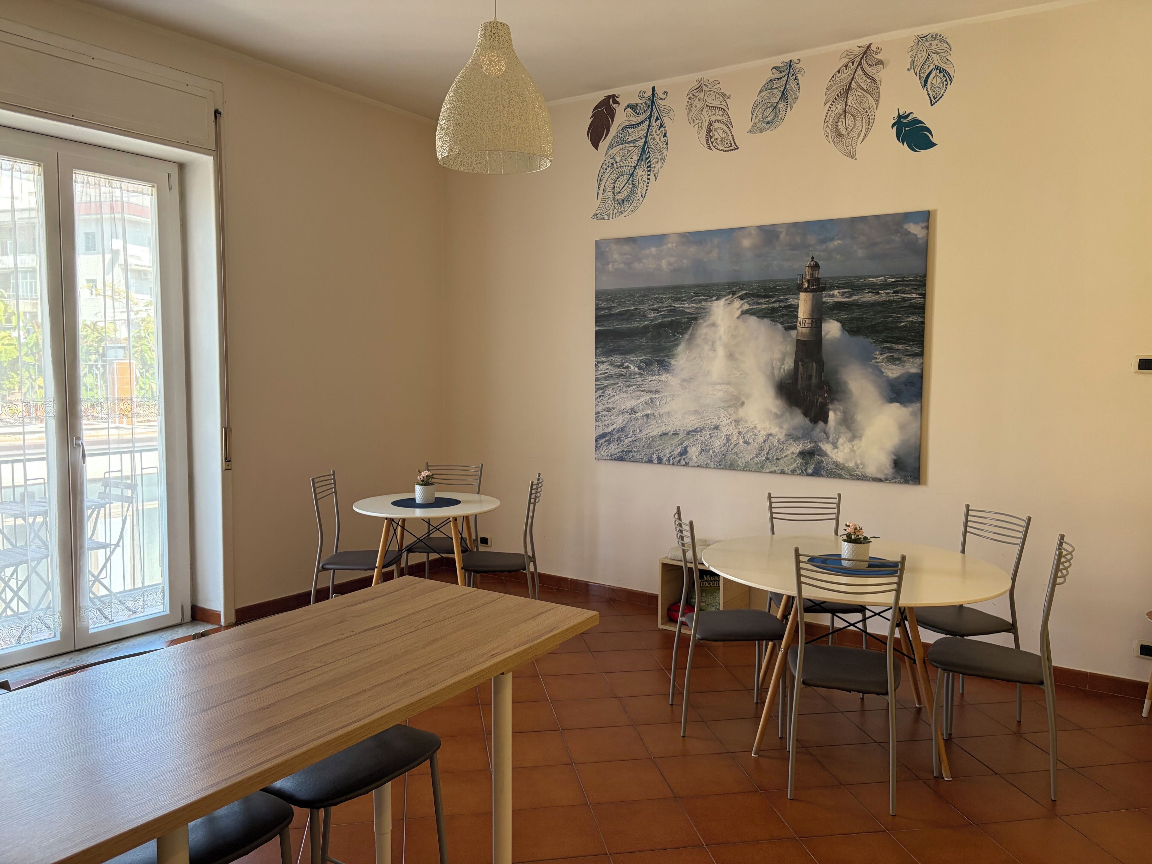 Un coin repas comprenant une table ronde, des chaises, un luminaire suspendu et un tableau représentant un phare, accroché au mur.