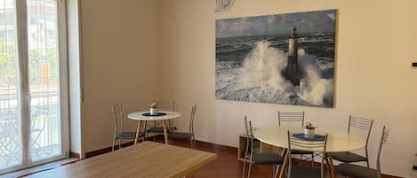 A dining area with a round table, chairs, a hanging light fixture, and a wall-mounted painting of a lighthouse.