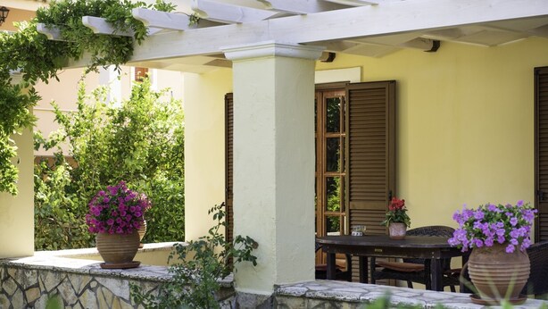 An outdoor patio area with a stone wall, a wooden table, and potted plants.