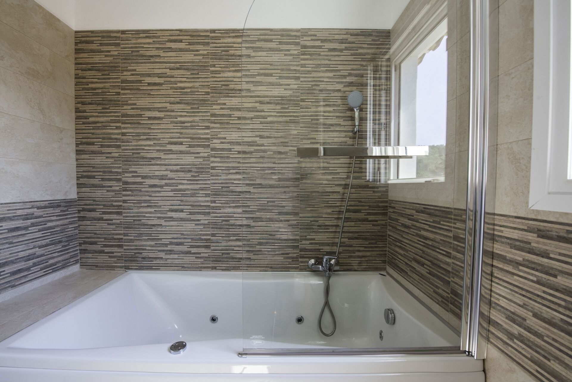 A modern bathroom with a glass-enclosed bathtub, a showerhead, and a window providing natural light.