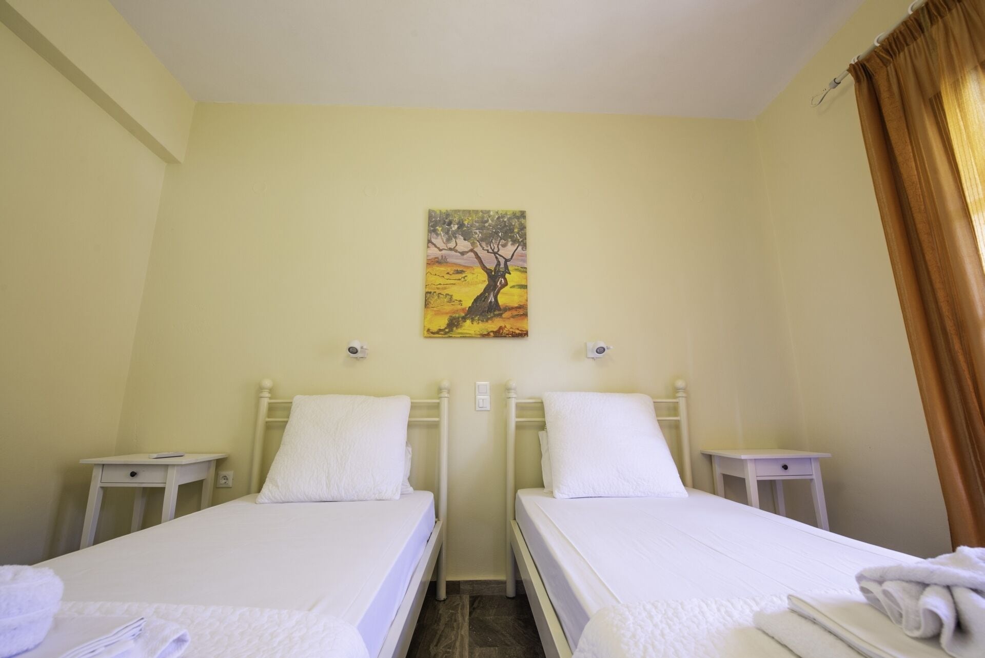 A twin room with two beds, a painting on the wall, and a window with curtains.