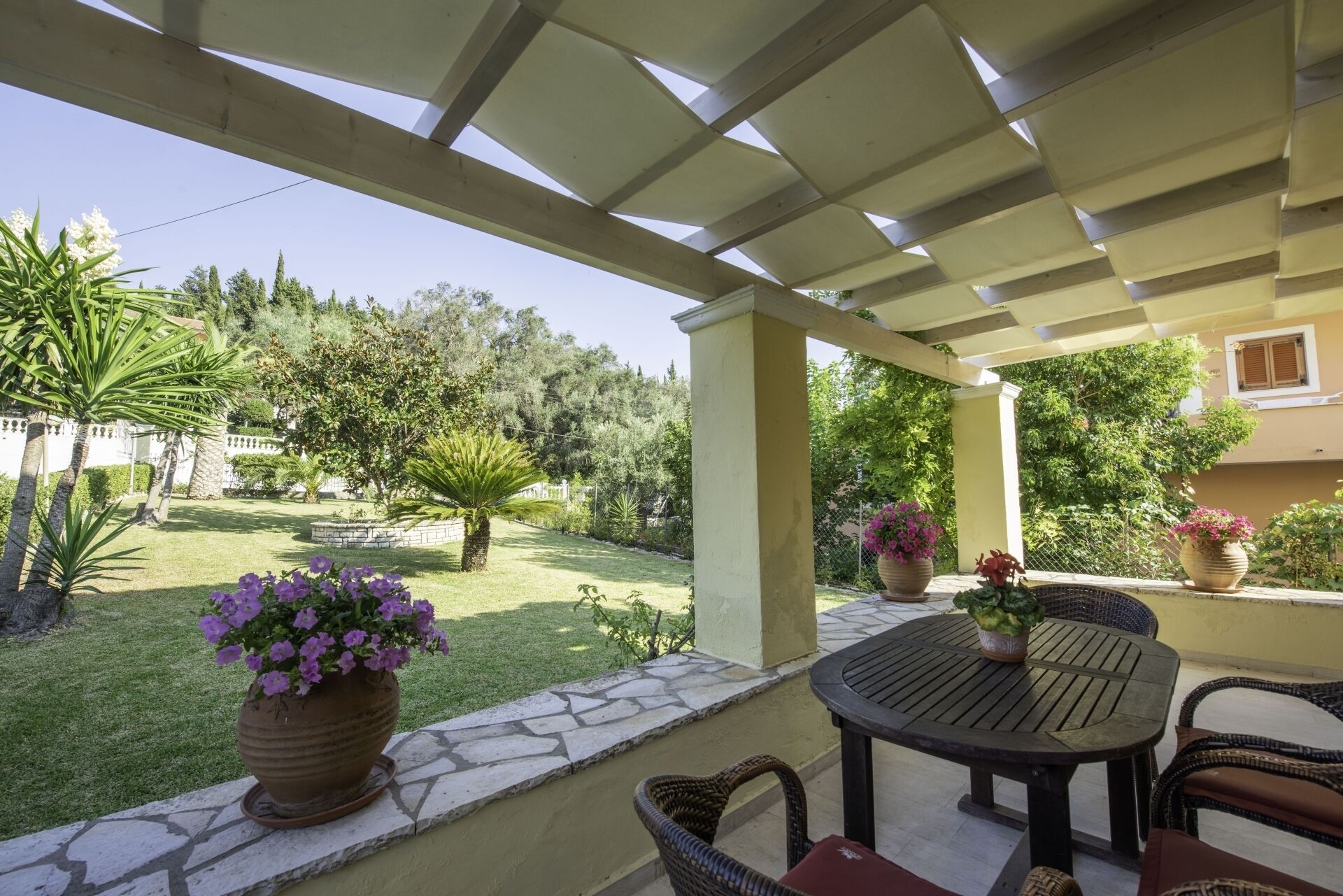 A covered patio with a stone wall, outdoor furniture, and potted plants.