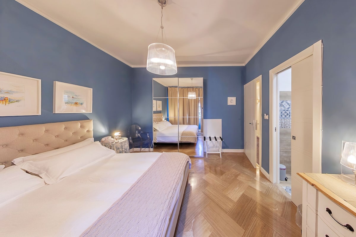 A bedroom with a large bed, a bedside table, a mirror, and a wardrobe.