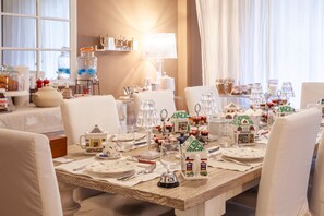 A dining table set with white tableware and festive decorations, including house-shaped items, in a well-lit room with a window and curtains. - Maison de Famille (Palermo)