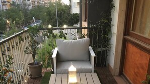Un balcon avec un canapé blanc et une petite table, entouré de plantes en pot et d’une balustrade.