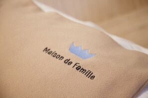 A pillow with embroidered text and a crown symbol. - Maison de Famille (Palermo)