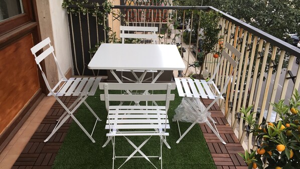 A balcony with a white table and chairs, surrounded by greenery and a wooden fence. - Maison de Famille (Palermo)