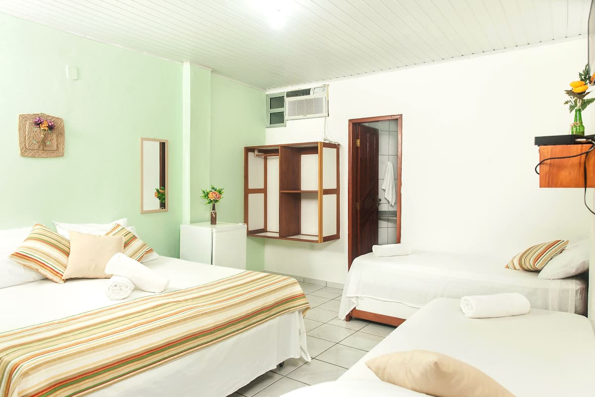 A hotel room with two beds, a small table, a mirror, and a wall-mounted air conditioner.