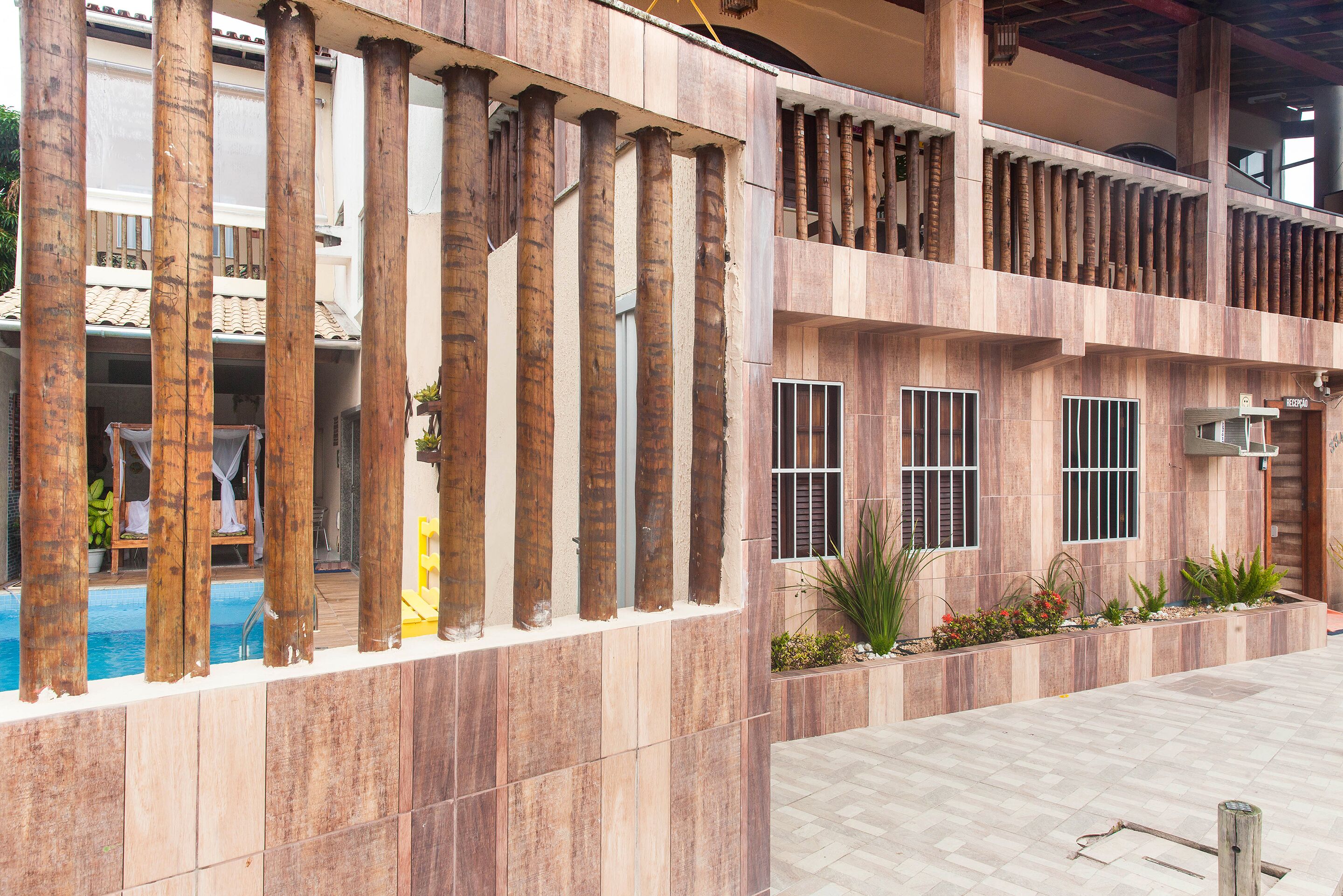 Un edificio con piscina, columnas de madera y un balcón.