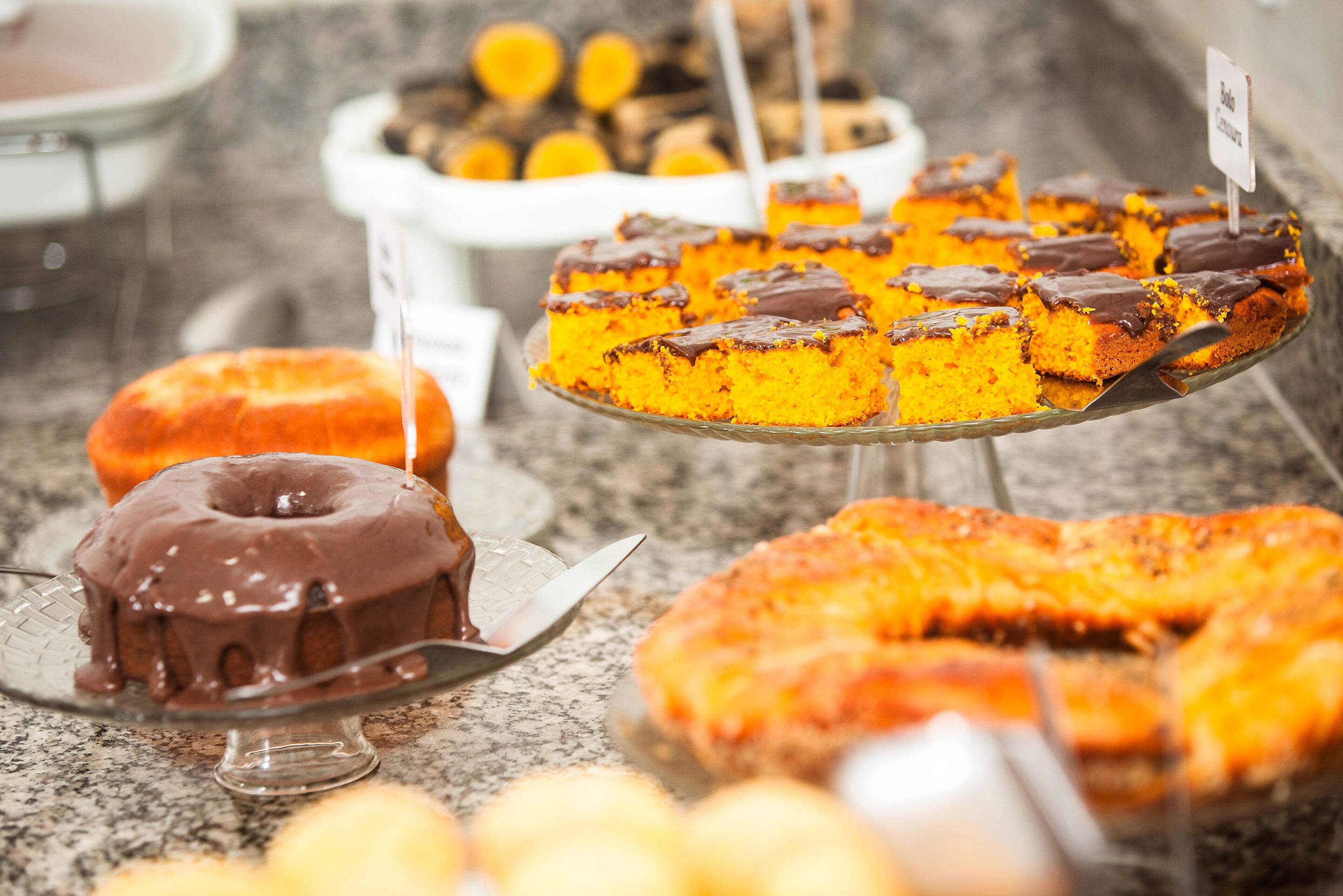 A variety of desserts on display, including a chocolate-covered bundt cake, a slice of pumpkin cake, and other baked goods.