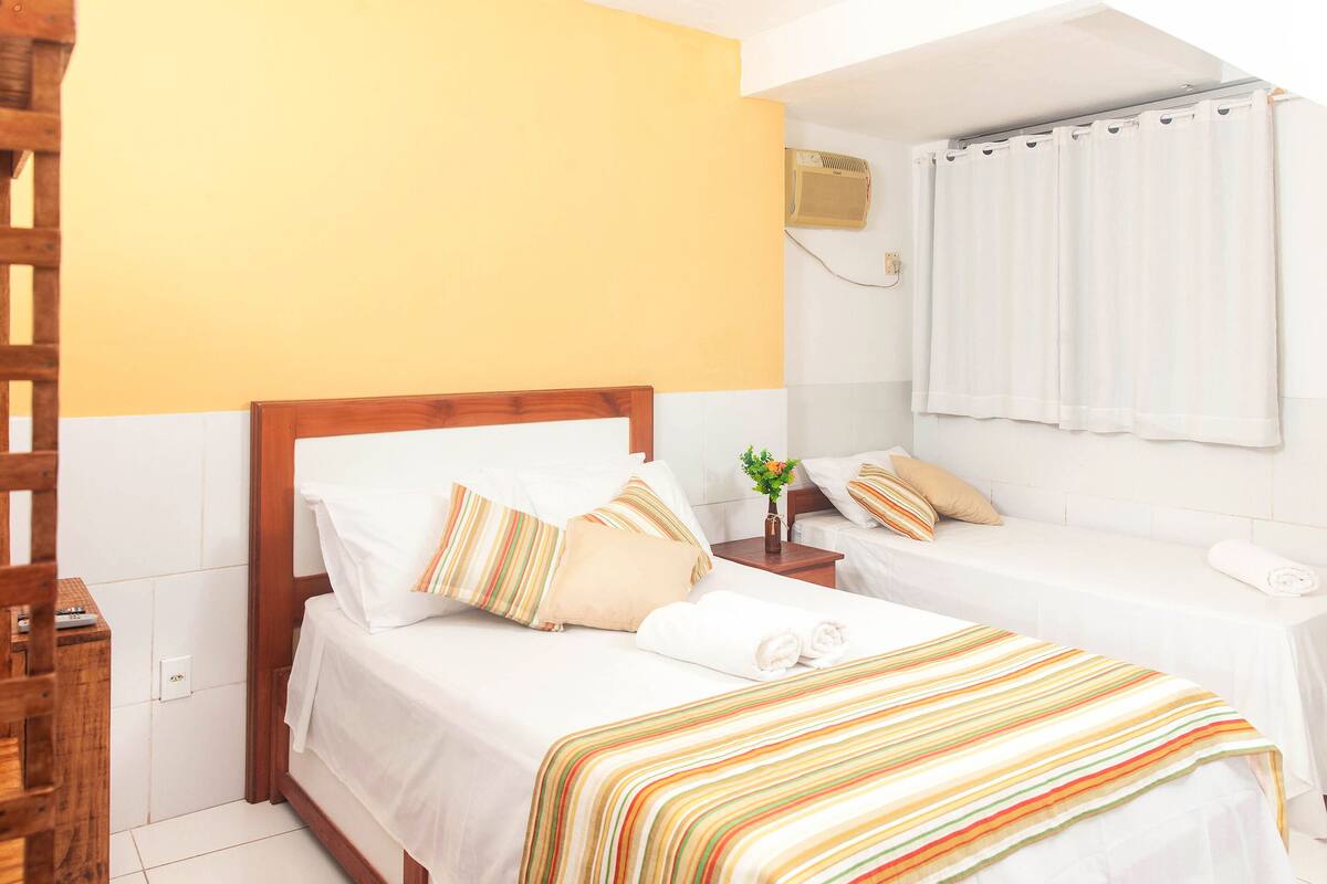 A hotel room with two beds, a wooden headboard, a bedside table with a vase, and a window with curtains.
