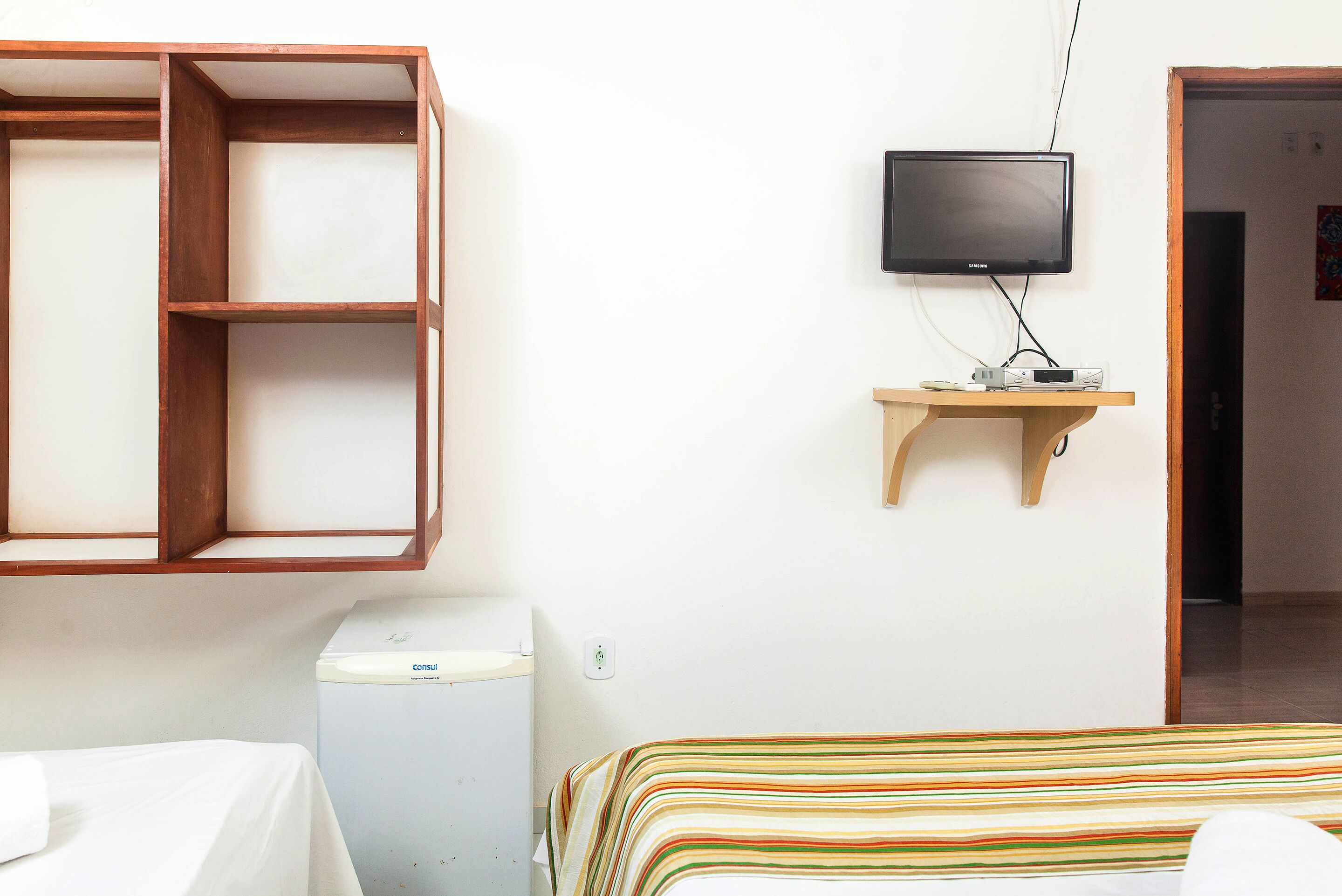Een kamer met een bed, een houten plank met een televisie, en een wit apparaat.