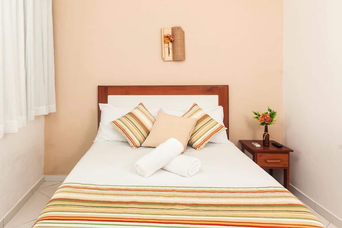 A neatly made bed with striped bedding, a wooden headboard, and a bedside table with a vase of flowers.