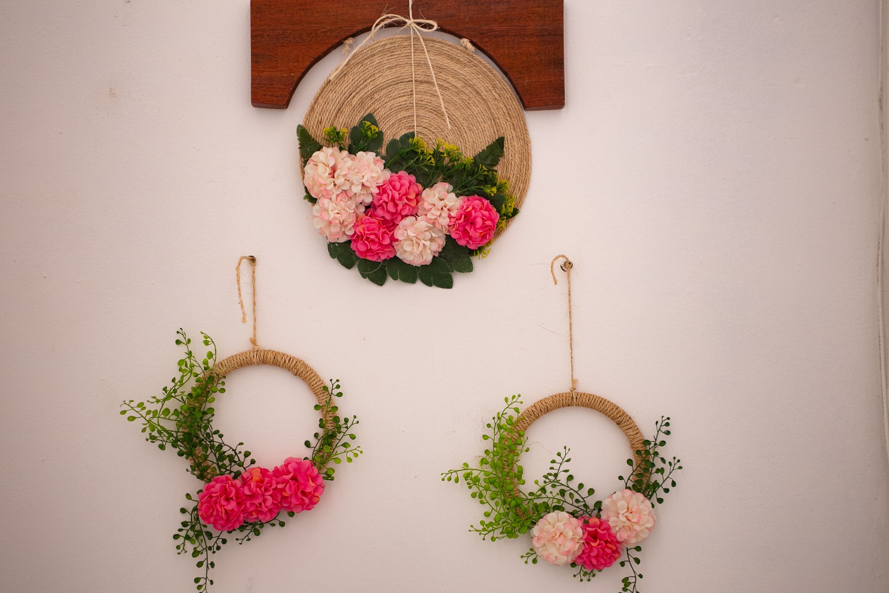 Una pared con dos adornos circulares tejidos, cada uno con follaje rosa y verde.