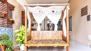 A wooden four-poster bed with a green patterned bedspread, surrounded by potted plants and a tiled floor. - Pousada Recanto do Mucugê (Porto Seguro)
