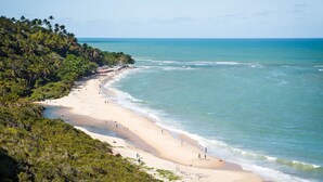 A beach with a sandy shore, clear blue water, and dense tropical vegetation. - Pousada Recanto do Mucugê (Porto Seguro)