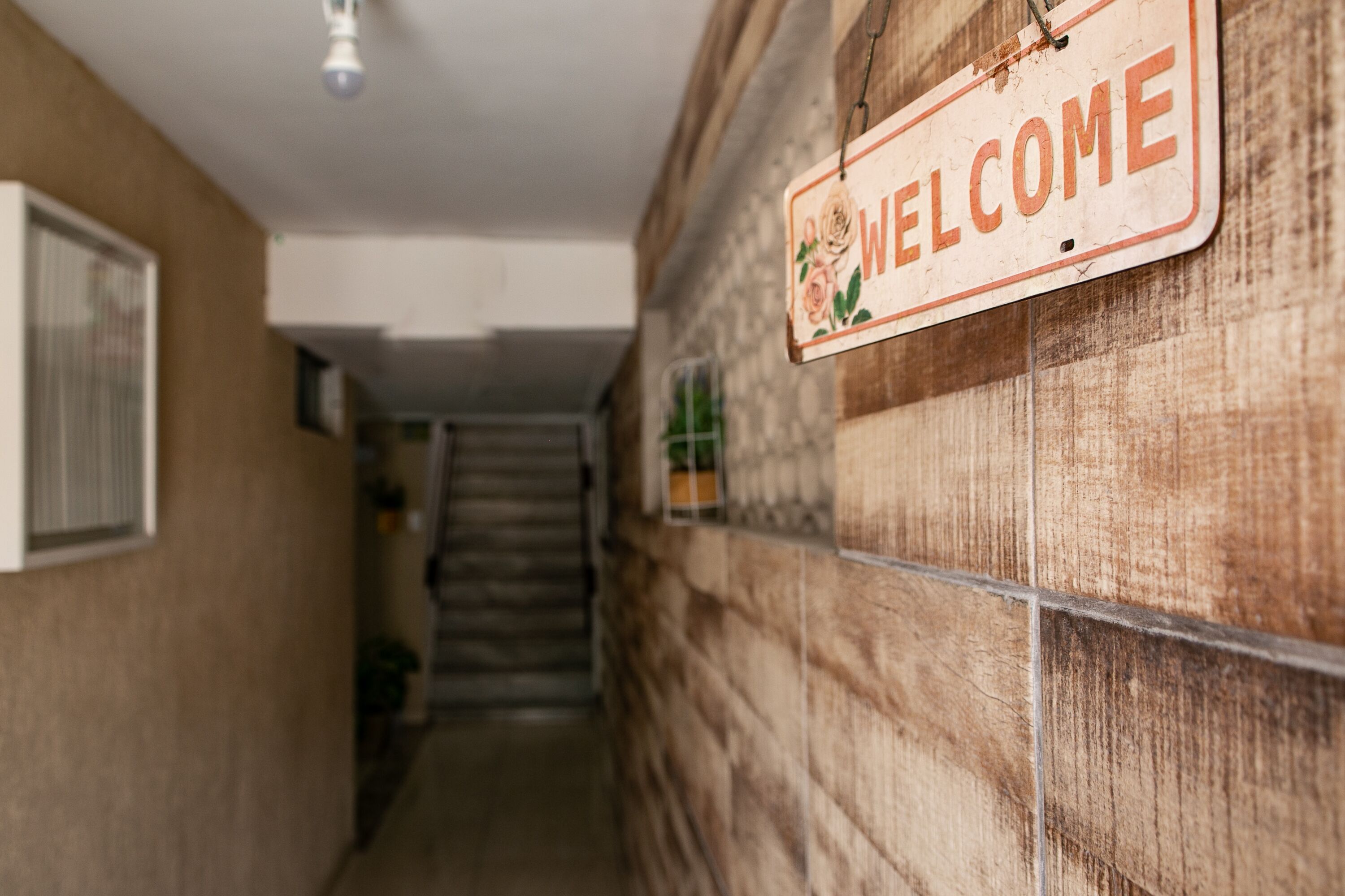 Een hal met een 'WELCOME' bord aan de muur, een trap en een raam aan de linkerkant.