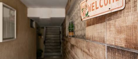 Een hal met een 'WELCOME' bord aan de muur, een trap en een raam aan de linkerkant.