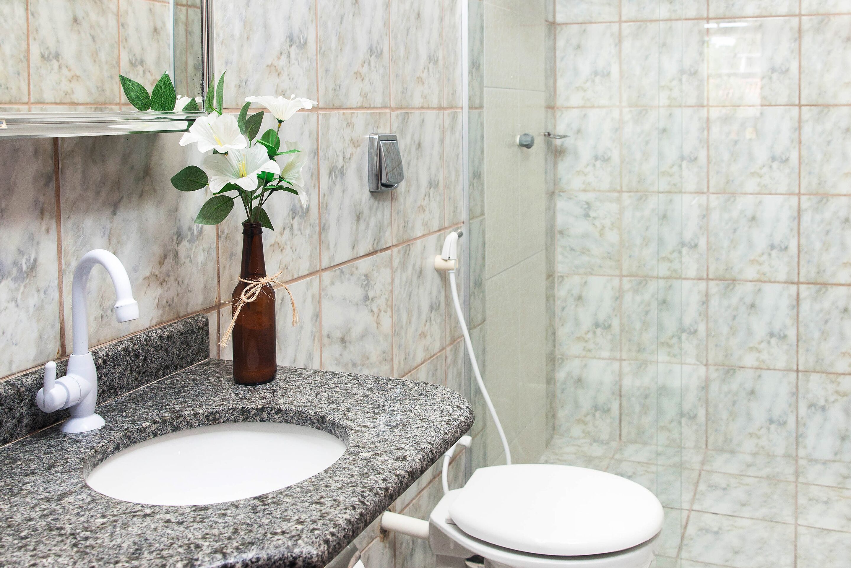 A bathroom with a granite countertop, a white sink, a toilet, and a mirror.