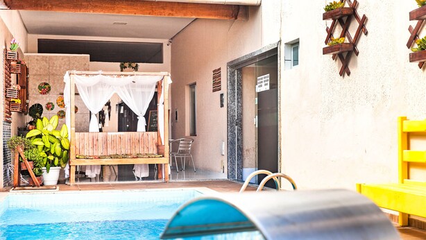 A pool area with a wooden bench, a white canopy, and potted plants. - Pousada Recanto do Mucugê (Porto Seguro)