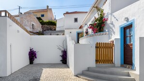 A cobblestone courtyard with white walls and blue doors, leading to a wooden staircase. - Carvoeira Surf & Family Villa (Mafra)