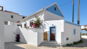 A white building with blue trim and a wooden door, featuring a cobblestone courtyard and a small garden with flowers. - Carvoeira Surf & Family Villa (Mafra)