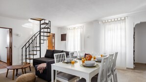 A modern living room with a white dining table set for four, a staircase, and a sofa. - Carvoeira Surf & Family Villa (Mafra)
