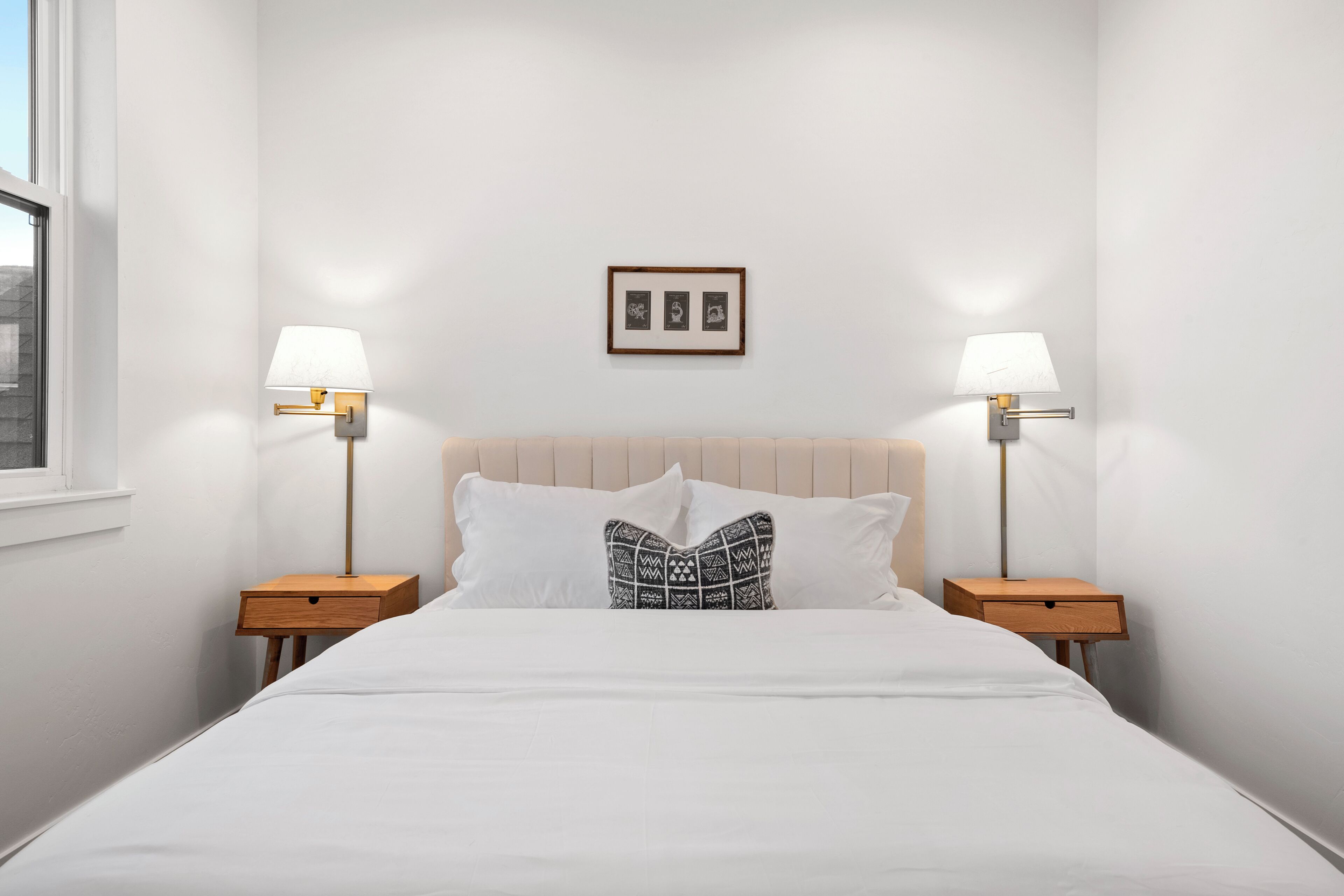 A neatly made bed with a patterned pillow, two bedside tables with lamps, and a framed picture on the wall.