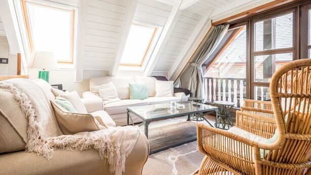 Ein gemütliches Schlafzimmer im Loft-Stil mit hohen Decken, Dachfenstern, einer Couch, einem Glastisch und einem Korbstuhl.