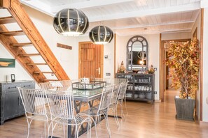 Un coin repas avec une table à plateau en verre, des chaises en fil de fer blanc et un escalier en bois.