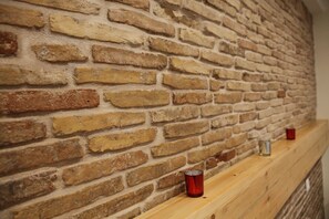 A brick wall with a wooden shelf holding two red glasses. - George Studio (Athens)