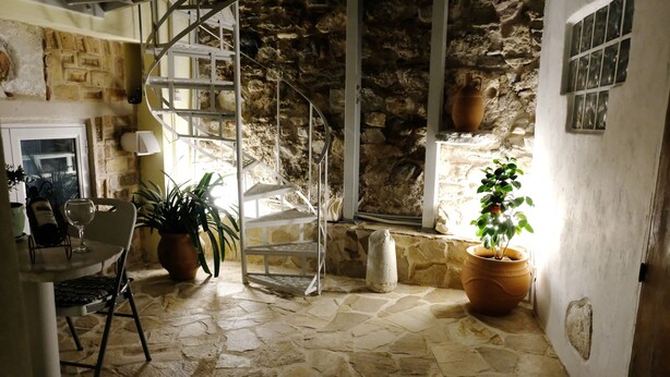 Um quarto com piso de pedra, uma escada em espiral, uma mesa com cadeiras e plantas em vasos.