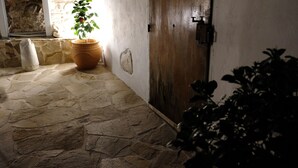 Corredor com piso de pedra, porta de madeira e um vaso de planta perto de uma janela.