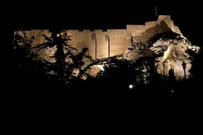 A large, illuminated stone structure at night, surrounded by trees. - George Studio (Athens)