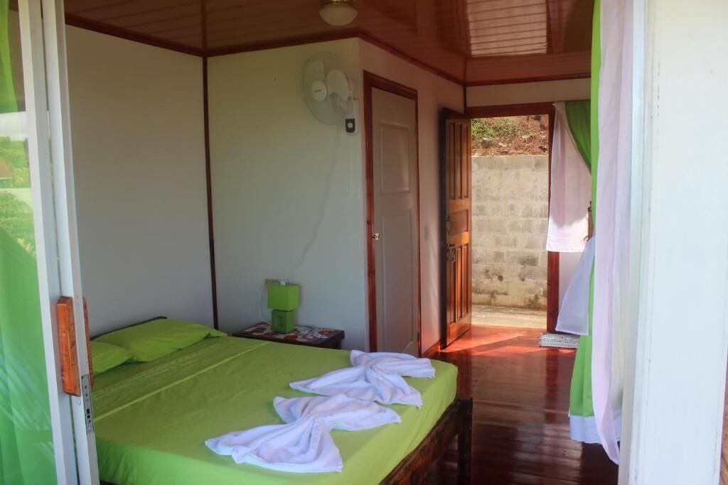 Una habitación con cama, mesita de noche, ventilador y vistas al exterior.
