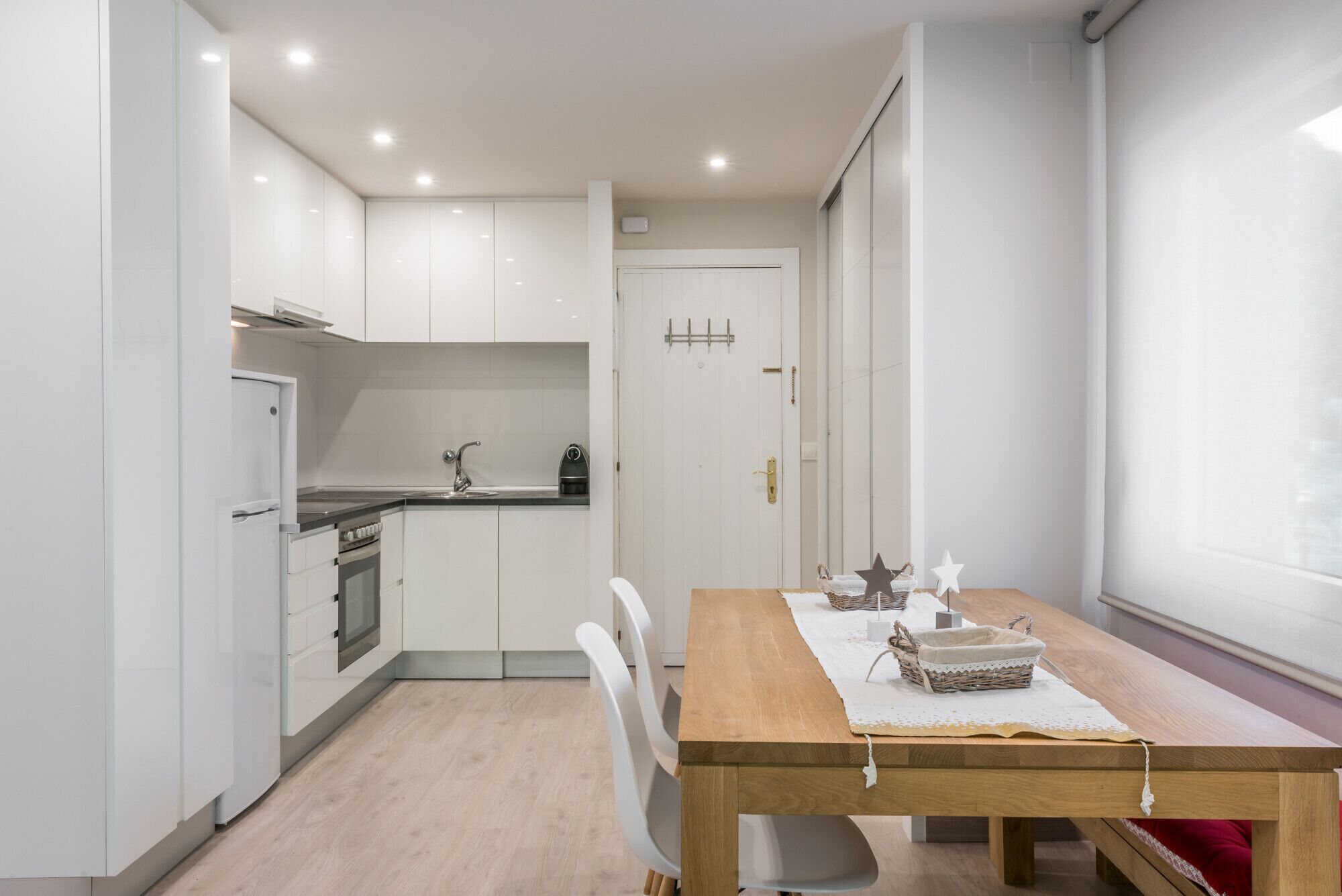 Una cocina moderna con armarios blancos, una mesa de comedor de madera y una ventana con cortinas.