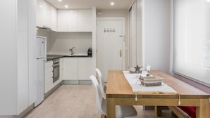 Una cocina moderna con armarios blancos, una mesa de comedor de madera y una ventana con cortinas.