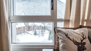 Una stanza con una finestra vista su un paesaggio innevato, un letto con un cuscino raffigurante la sagoma di un cervo, e una tenda parzialmente socchiusa.