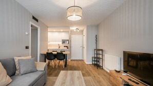 Un soggiorno moderno con un divano grigio, un tavolino in legno, un mobile TV e una zona pranzo con una cucina sullo sfondo.