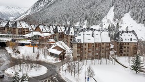 Una località turistica innevata con diversi edifici, una seggiovia e montagne sullo sfondo.