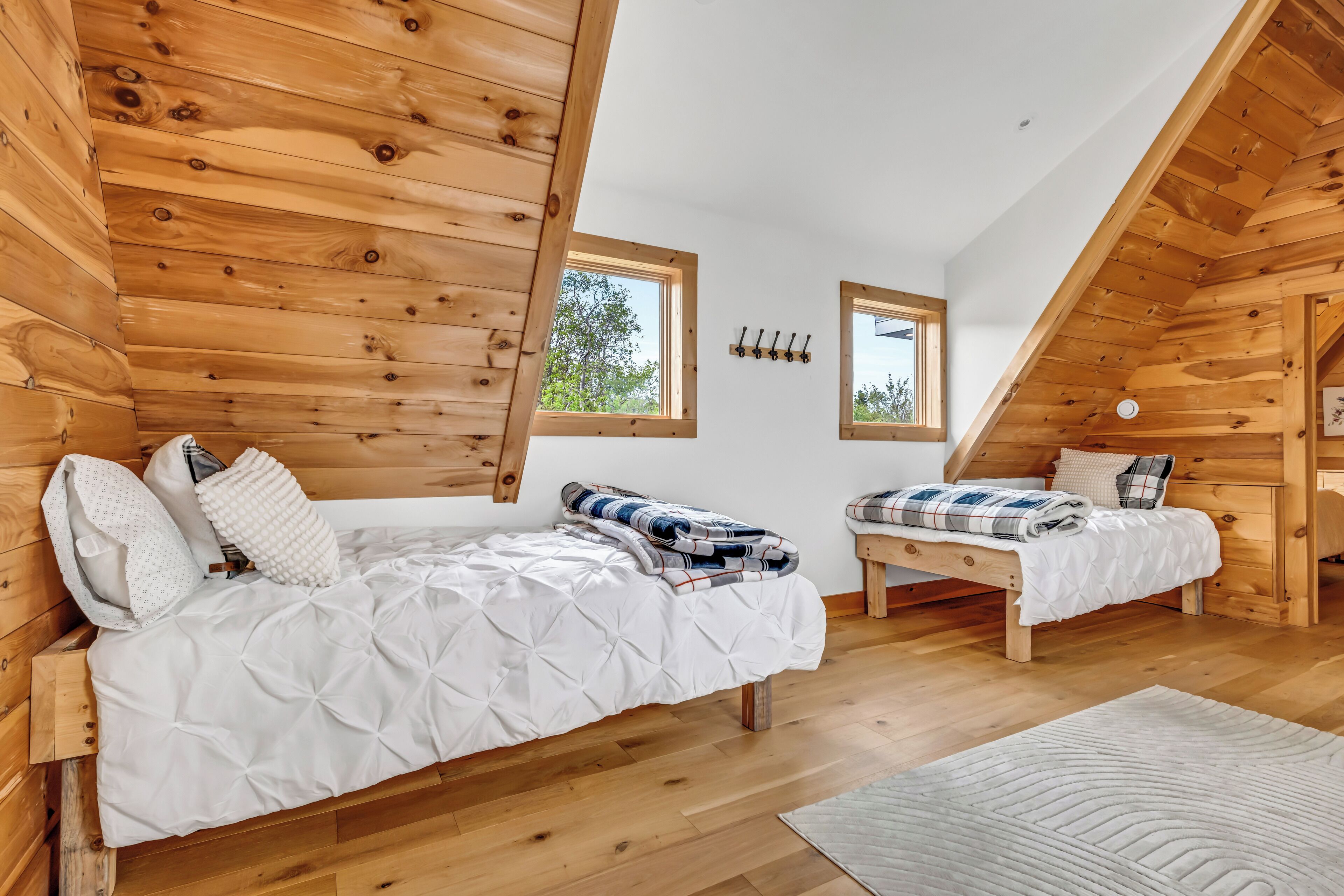 A wooden cabin bedroom with two bunk beds, a white quilted bedspread, and a wooden ceiling.