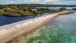 A coastal area with a sandy beach, clear water, and houses in the background. - Beach Front Estate Custom Timber Frame Home on Cleveland Beach 72 (Hubbards)