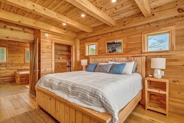 Ein Schlafzimmer einer Holzhütte mit einem großen Bett, Nachttischen und einem Fenster mit einem Gemälde.