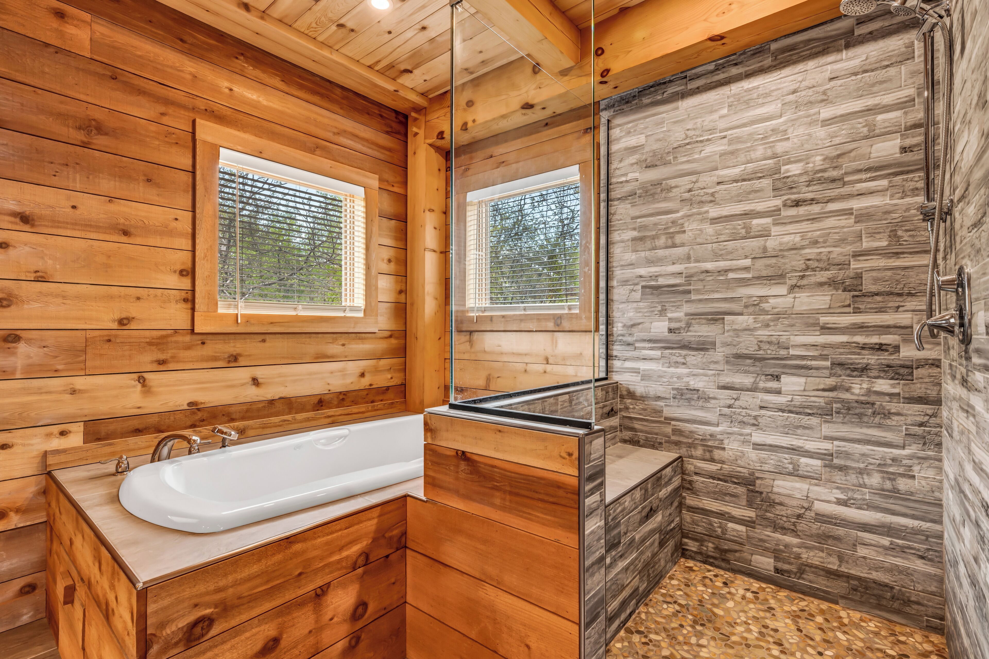 A wooden cabin bathroom with a bathtub, a shower, and a large mirror.